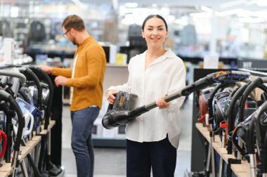 Bir kaç genç müşteri ev aletleri mağazasından elektrikli süpürge seçiyor..
