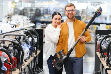 Çömelmiş çiftler ve satın almak istedikleri elektrik süpürgesine bakıyorlar. Teknoloji mağazası içi.