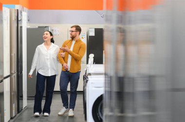 Genç çift, memnun müşteriler eşyalar mağazasında buzdolabı seçiyor..