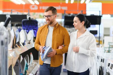 Elektronik mağazasında dikilen çift ütü yapmak için elektrikli ütü seçiyor. Ev işleri.