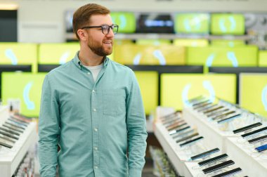 Bir adam bir elektronik mağazasında cep telefonlarının yanında duruyor.