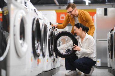 Mutlu genç çift mağazadan çamaşır makinesi alıyor..