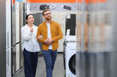 Genç çift, memnun müşteriler eşyalar mağazasında buzdolabı seçiyor..