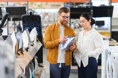 Elektronik mağazasında dikilen çift ütü yapmak için elektrikli ütü seçiyor. Ev işleri.