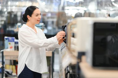 Genç bir kadın hipermarkette yeni bir mikrodalga fırın seçti..