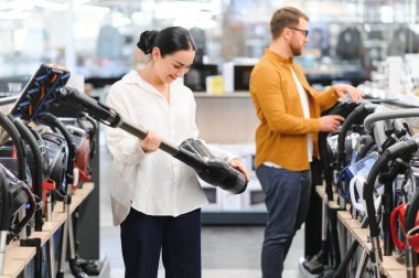 Bir kaç genç müşteri ev aletleri mağazasından elektrikli süpürge seçiyor..