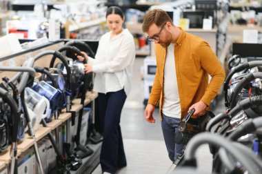 Bir kaç genç müşteri ev aletleri mağazasından elektrikli süpürge seçiyor..