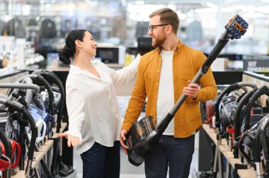 Bir kaç genç müşteri ev aletleri mağazasından elektrikli süpürge seçiyor..