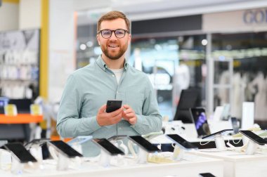Mutlu genç adam teknoloji mağazasında yeni bir cep telefonu seçiyor..