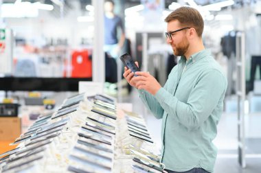 Mutlu genç adam teknoloji mağazasında yeni bir cep telefonu seçiyor..