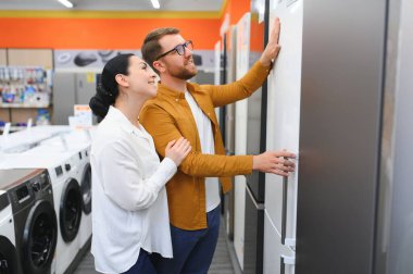 Genç çift, memnun müşteriler eşyalar mağazasında buzdolabı seçiyor..