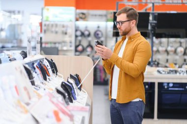 Sakallı stil sahibi bir adam, elektronik budama makineleri ve ustura ile vitrinde dikilirken bir seçim yapar. Mağazadan yeni bir budayıcı alıyorum..