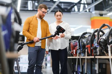 Bir kaç genç müşteri ev aletleri mağazasından elektrikli süpürge seçiyor..