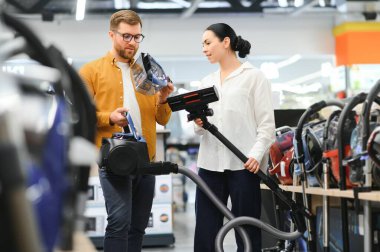 Bir kaç genç müşteri ev aletleri mağazasından elektrikli süpürge seçiyor..