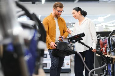 Bir kaç genç müşteri ev aletleri mağazasından elektrikli süpürge seçiyor..