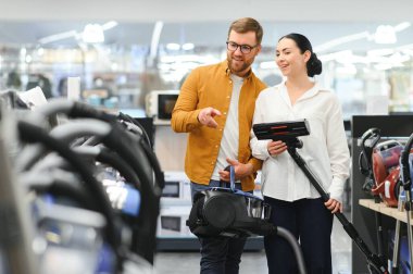 Bir kaç genç müşteri ev aletleri mağazasından elektrikli süpürge seçiyor..