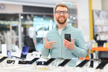 Mutlu genç adam teknoloji mağazasında yeni bir cep telefonu seçiyor..