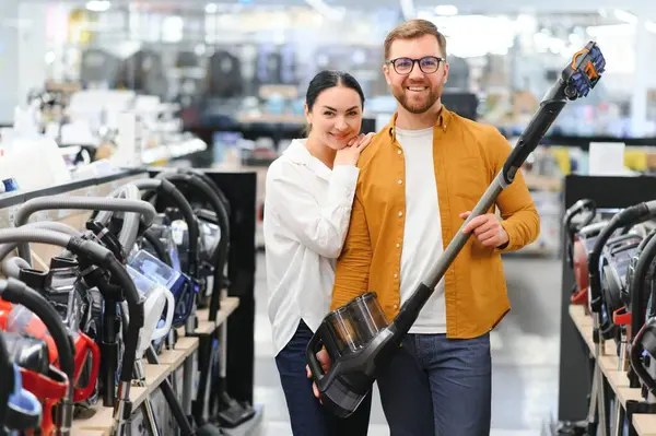 Çömelmiş çiftler ve satın almak istedikleri elektrik süpürgesine bakıyorlar. Teknoloji mağazası içi.