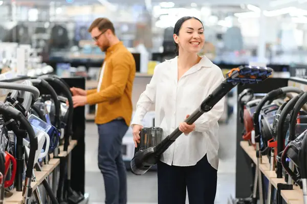 Bir kaç genç müşteri ev aletleri mağazasından elektrikli süpürge seçiyor..