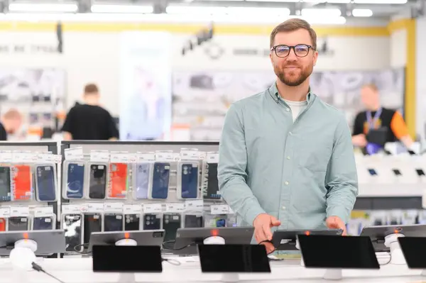 stock image Portrait of happy satisfied young bearded man with eyeglasses testing a tablet in a tech store.