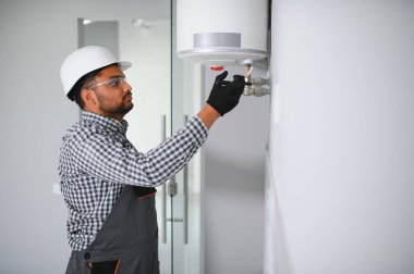 Hintli tesisatçı kazan ya da su ısıtıcısını tamir ederken tornavida kullanıyor, apartmanda ısıtma sistemi üzerinde çalışıyor..