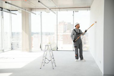 Hintli bir apartman tamircisi silindirle beyaz bir duvar boyuyor..