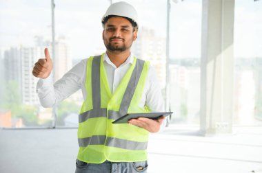 İnşaat alanında miğfer takan yakışıklı genç Hintli inşaat mühendisi ya da mimarın portresi..