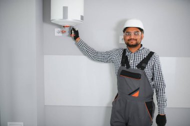 Hintli tesisatçı kazan ya da su ısıtıcısını tamir ederken tornavida kullanıyor, apartmanda ısıtma sistemi üzerinde çalışıyor..