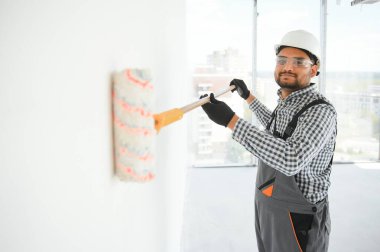 Hintli bir apartman tamircisi silindirle beyaz bir duvar boyuyor..