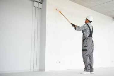 Hintli bir apartman tamircisi silindirle beyaz bir duvar boyuyor..