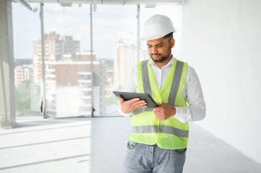 Hintli şantiye müdürü miğfer takıyor, inşaat alanında düşünüyor. Karışık ırk el işçisinin ya da mimarın portresi.