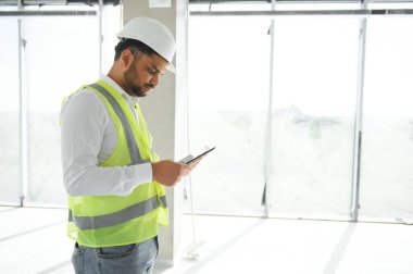 Hintli şantiye müdürü miğfer takıyor, inşaat alanında düşünüyor. Karışık ırk el işçisinin ya da mimarın portresi.