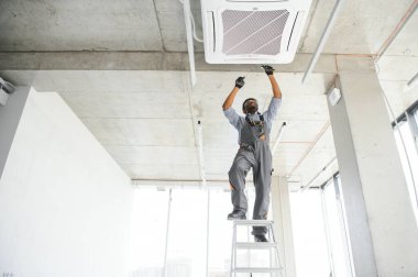 Afrikalı Amerikalı elektrikçi içeride klima tamir ediyor..