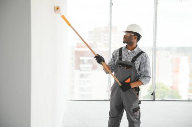 Afrikalı bir adam silindirle beyaz bir duvar boyuyor. İç kısmın tamiri.