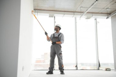 Afrikalı bir adam silindirle beyaz bir duvar boyuyor. İç kısmın tamiri.