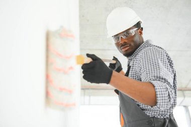 Afrikalı bir adam silindirle beyaz bir duvar boyuyor. İç kısmın tamiri.