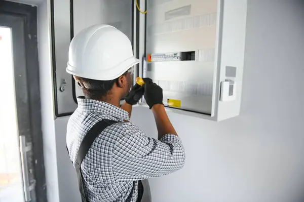 stock image African american electrician Repairing electricity switchboard.