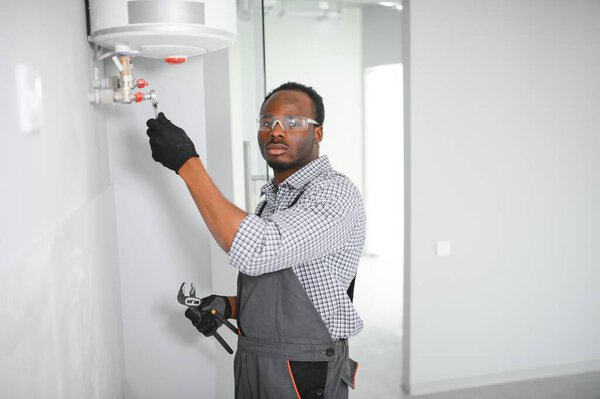 Young African Male Plumber Repairing Boiler Stock Photo