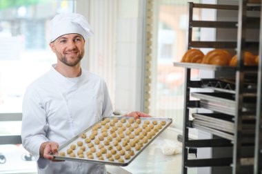 Genç fırıncı elinde taze kurabiyelerle dolu bir tepsi tutuyor..