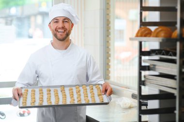 Genç fırıncı elinde taze kurabiyelerle dolu bir tepsi tutuyor..