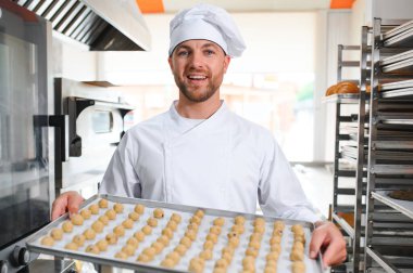 İyi kalitede. Steril giysi parlak gıda fabrikasında ayakta olgun neşeli erkek çalışanın resmini. Tepsi ile taze kurabiye dolu tutarak ve kalitesi iyidir eliyle işaret.