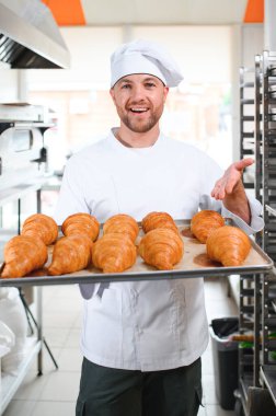 Üretim, taze pişmiş kruvasanlar dolu üniforma holding tepsisinde yakışıklı baker.