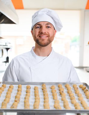 Genç fırıncı elinde taze kurabiyelerle dolu bir tepsi tutuyor..