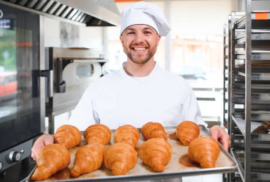 Baker holding tepsi ile ekmek fırınları taze pişmiş kruvasanlar gülümseyen.