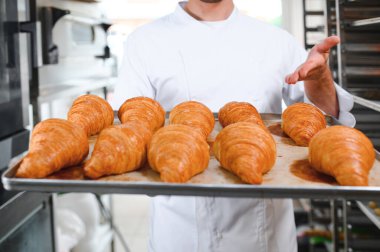 Baker holding tepsi ile ekmek fırınları taze pişmiş kruvasanlar gülümseyen.