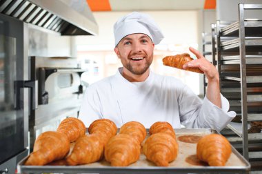 Üretim, taze pişmiş kruvasanlar dolu üniforma holding tepsisinde yakışıklı baker.