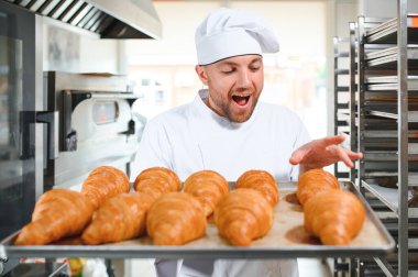 Üretim, taze pişmiş kruvasanlar dolu üniforma holding tepsisinde yakışıklı baker.