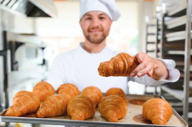 Üretim, taze pişmiş kruvasanlar dolu üniforma holding tepsisinde yakışıklı baker.