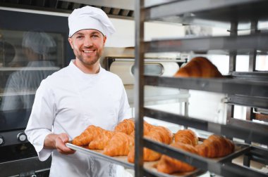 Baker holding tepsi ile ekmek fırınları taze pişmiş kruvasanlar gülümseyen.