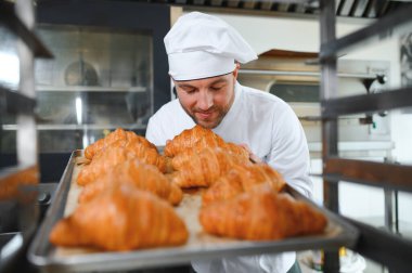 Baker holding tepsi ile ekmek fırınları taze pişmiş kruvasanlar gülümseyen.